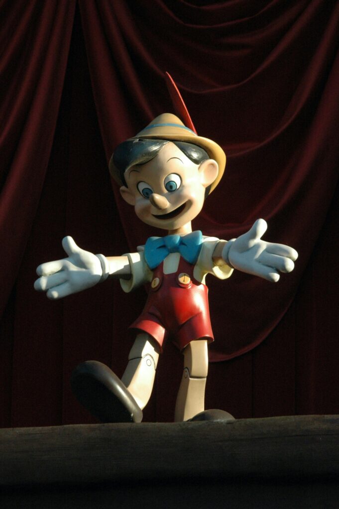 Charming wooden Pinocchio doll posed against a dramatic red curtain backdrop.